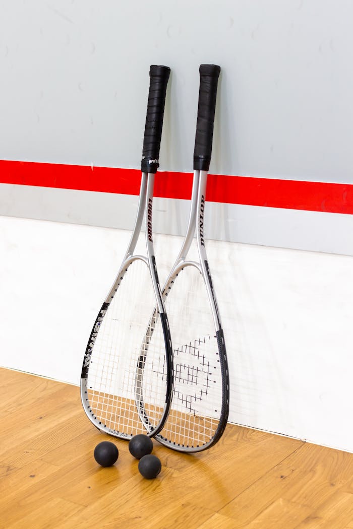 Two squash rackets with balls against a red line wall on a wooden squash court.